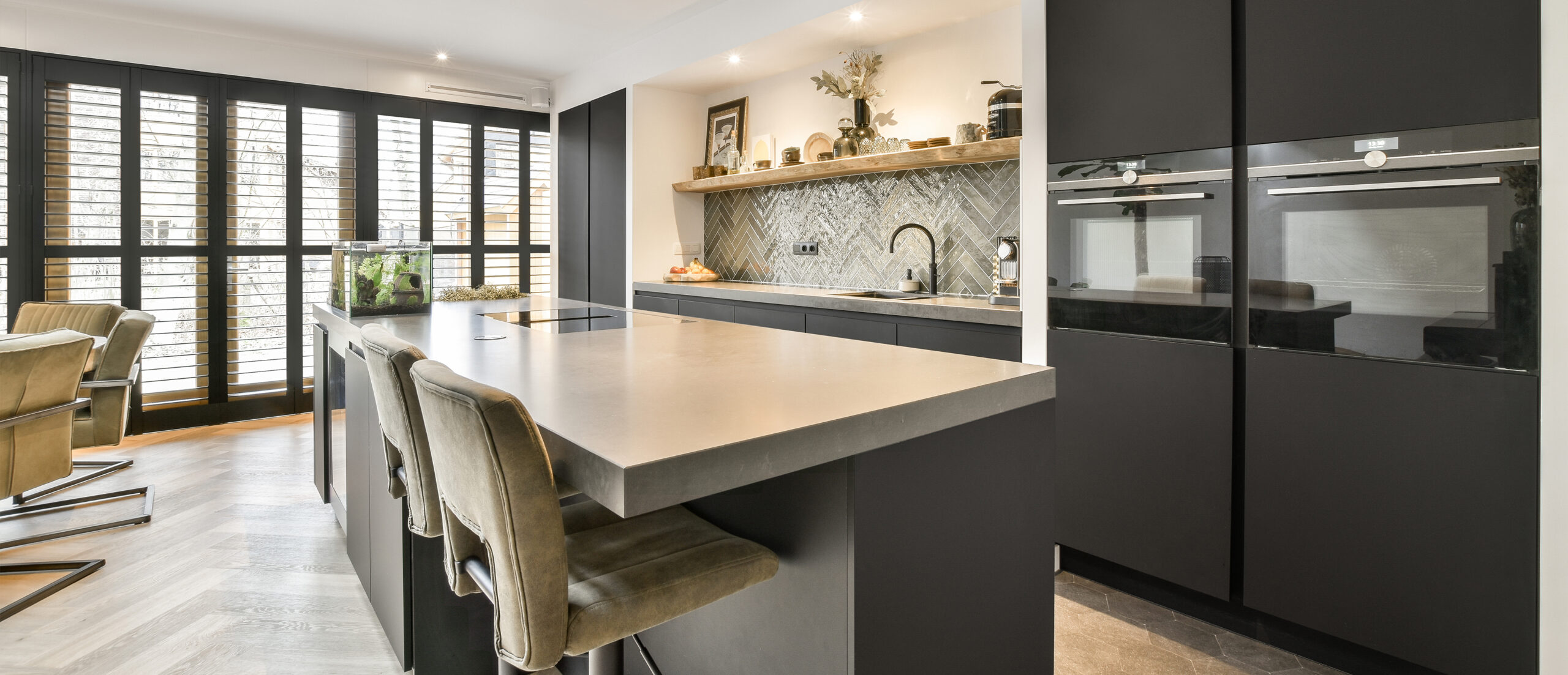 Keuken met marmeren werkblad, donkere kastdeuren en veel natuurlijk licht dankzij een glazen dak, afgewerkt door JRC Afbouw.