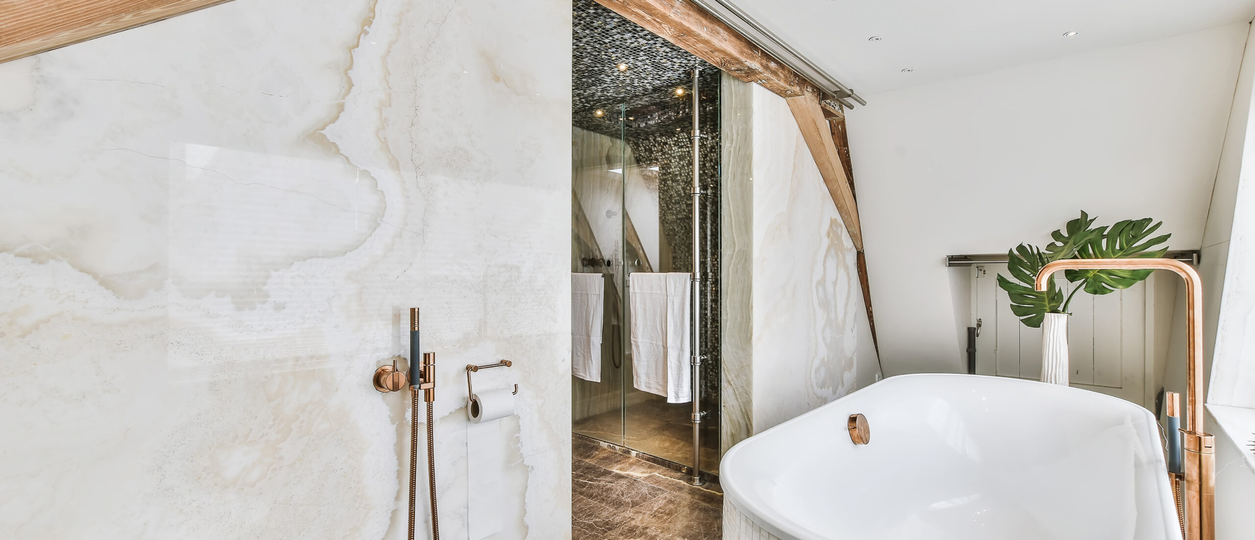 Luxe badkamer met marmeren muur, vrijstaand bad en koperen details door JRC Afbouw.