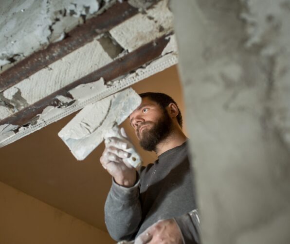 Een vakman met baard van JRC Afbouw brengt met precisie stucwerk aan op een deurkozijn voor een strakke afwerking