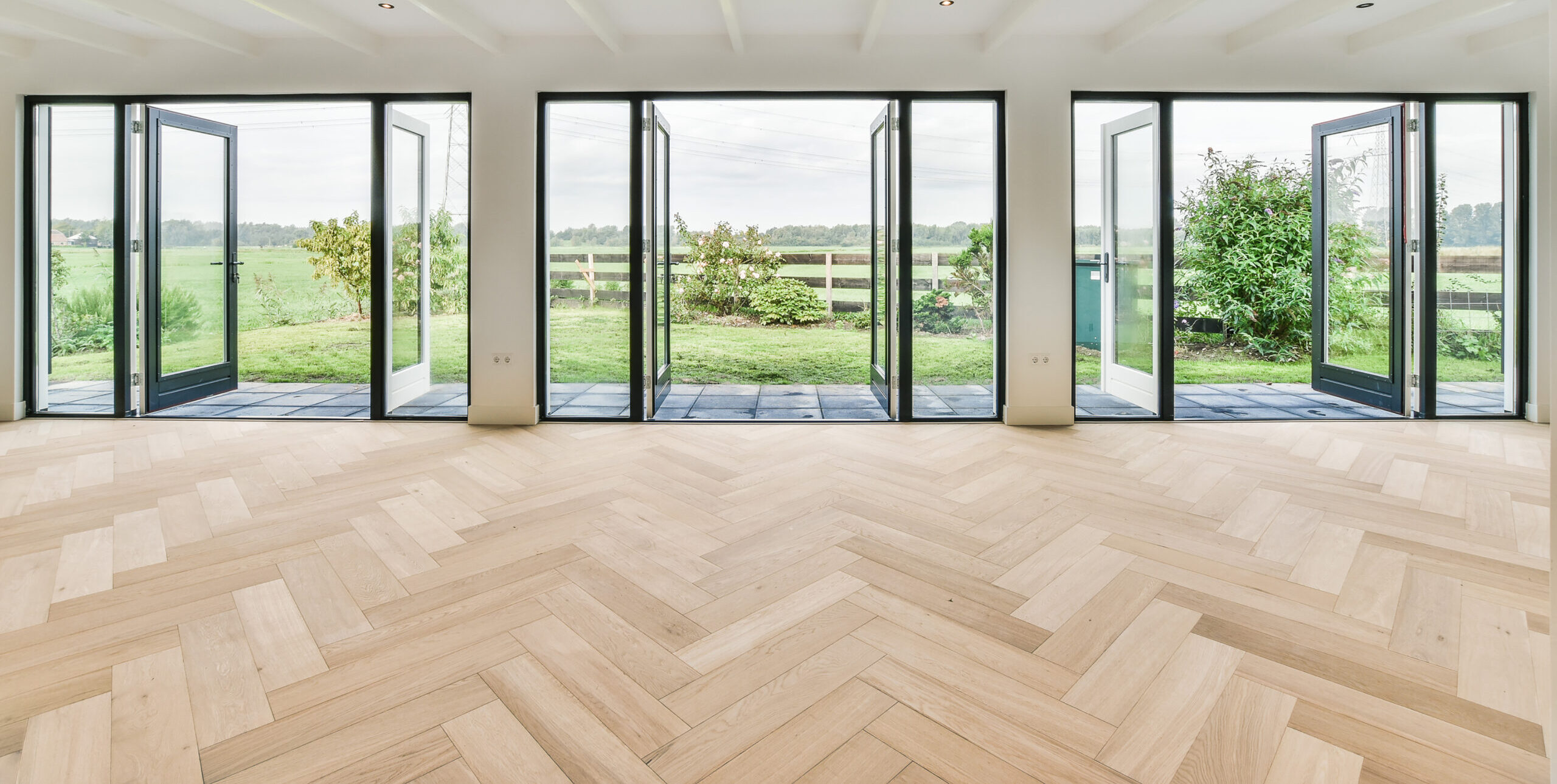 Lichte visgraatvloer in een moderne woonkamer met openslaande deuren naar de tuin, afgewerkt door JRC Afbouw